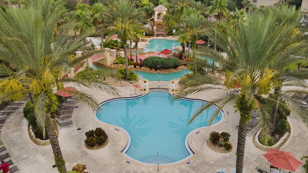 Ein Resort mit einem zentralen Schwimmbad, Palmen und einem kleinen Turm.