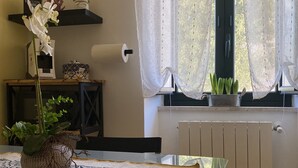 Ein Essbereich mit einem Tisch für zwei Personen, einem Blumentopf und einem Fenster mit durchsichtigen Vorhängen.