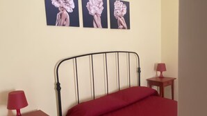 Ein Schlafzimmer mit einem Bett, einem Nachttisch, einer Lampe und drei Wandbildern mit Blumenmotiven.