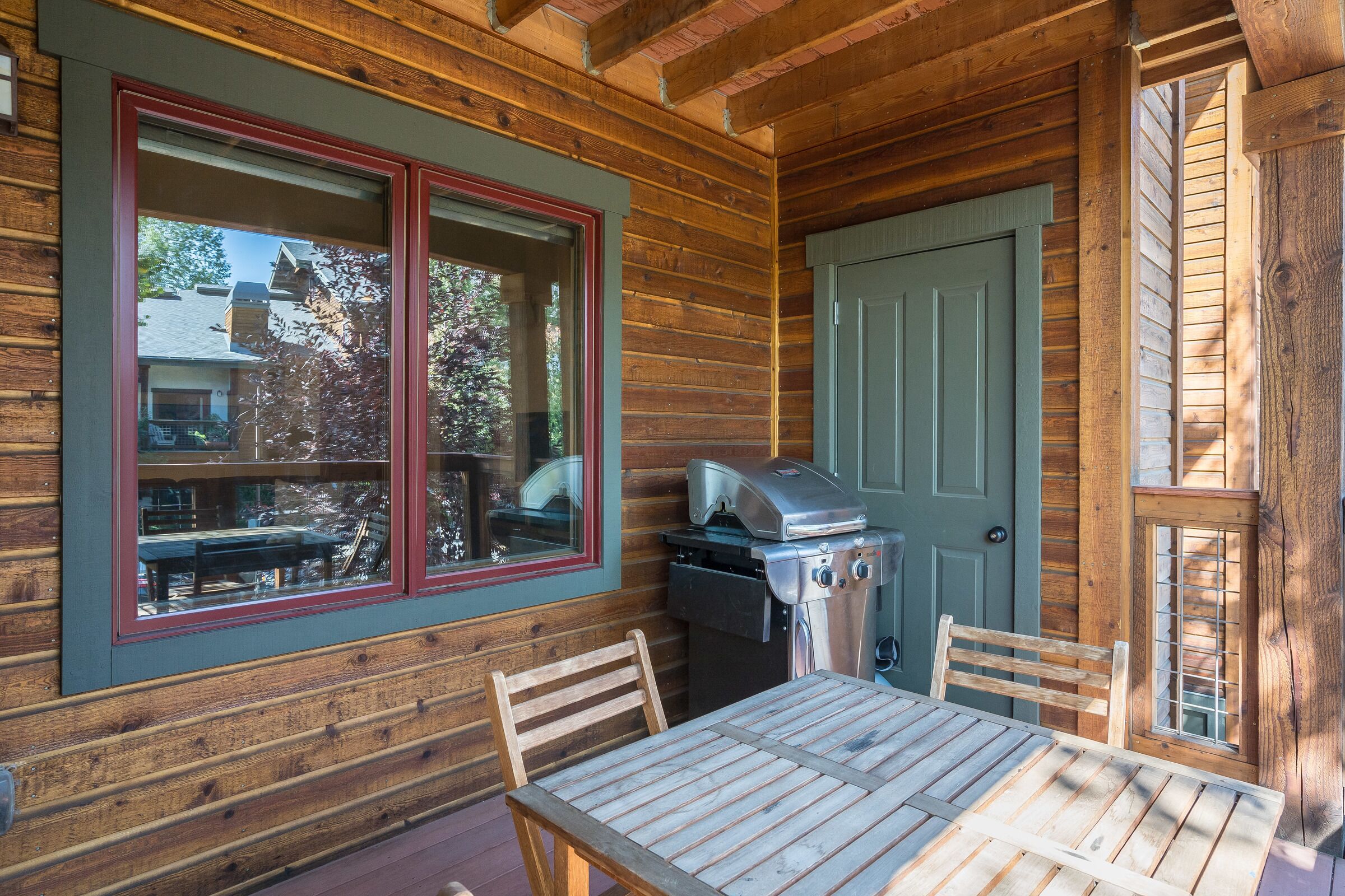 A wooden cabin with a dining table and chairs, a grill, and a window with a red frame.