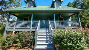 A two-story house with a green roof, a front porch with a railing, and a staircase leading to the entrance.
