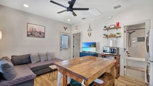 Una sala de estar moderna con una mesa de comedor de madera, un sofá gris y un ventilador de techo.