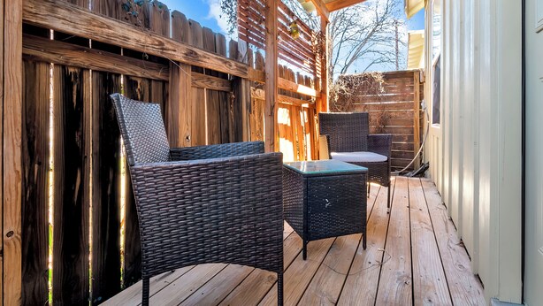 Una terraza de madera con mobiliario de mimbre, incluyendo dos sillas y una mesita.