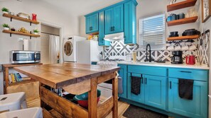 A kitchen with teal cabinets, a wooden table, a microwave, a washing machine, and a stove. - SA Urban Tiny House  (San Antonio)