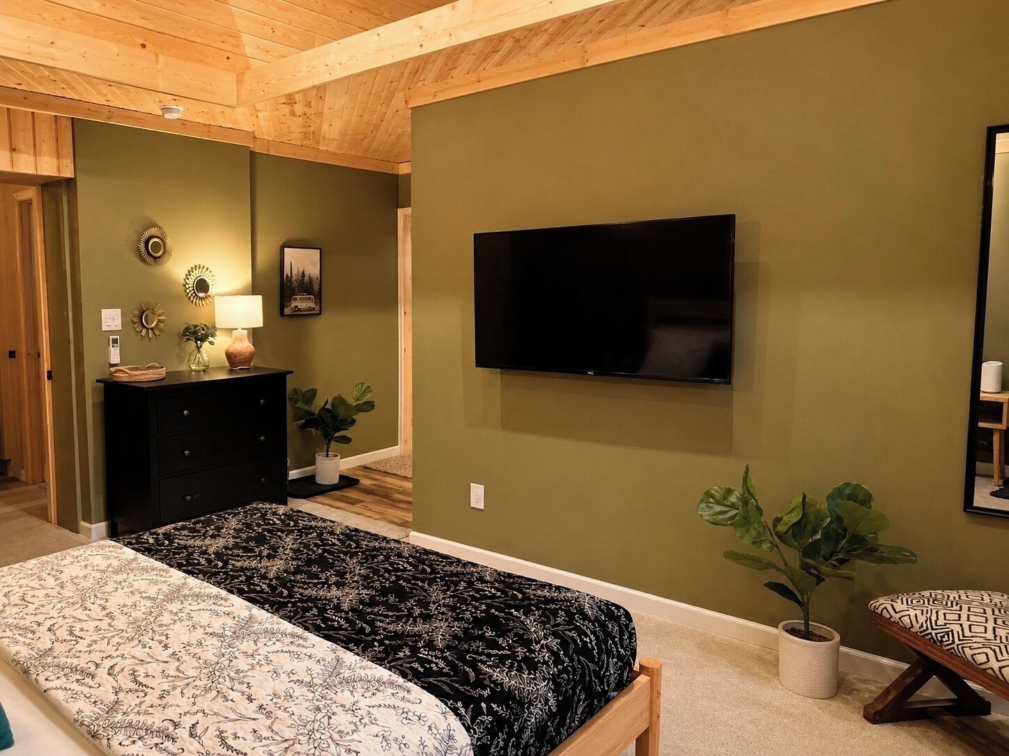 Een slaapkamer met een bed, een dressoir, een televisie en potplanten.