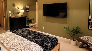 Een slaapkamer met een bed, een dressoir, een televisie en potplanten.