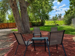 Un espace extérieur aménagé avec quatre chaises et une table, entouré d’arbres et d’une pelouse.