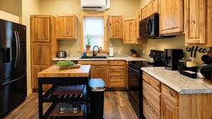 A kitchen with wooden cabinets, a black refrigerator, a microwave, a coffee station, and a window with blinds. - Remodeled 1890 Home with Large Fenced Yard  (Trinidad)