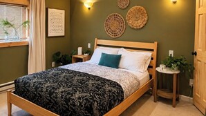 A wooden bed in a room with a green wall, two wall sconces, and a small round table with a plant. - Remodeled 1890 Home with Large Fenced Yard  (Trinidad)
