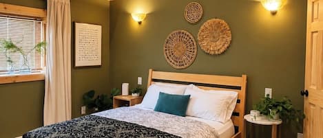 Ein hölzernes Bett in einem Zimmer mit grüner Wand, zwei Wandleuchten und einem kleinen, runden Tisch mit einer Pflanze.
