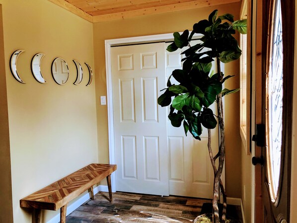Un couloir avec un banc en bois, une porte blanche et une plante en pot.