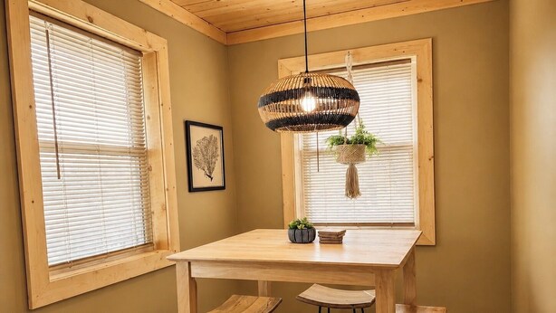 A dining area with a wooden table, four chairs, a hanging light fixture, and a window with a hanging plant. - Remodeled 1890 Home with Large Fenced Yard  (Trinidad)
