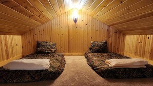 A room with two beds, each with a camouflage-patterned mattress and pillows, and a carpeted floor. - Turkey Roost At Creekside Resort (Clearville)
