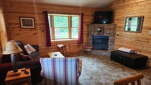 L’intérieur d’un chalet accueillant, avec une cheminée en pierre, des murs en bois, un canapé confortable et un fauteuil à rayures.