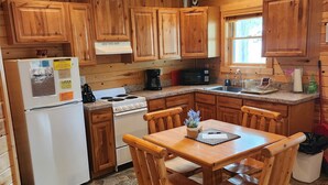 Une cuisine aménagée dans le style d’un chalet en bois, avec un sol carrelé en pierre, des meubles de rangement en bois, un réfrigérateur blanc, une cuisinière et une table à manger avec des chaises.