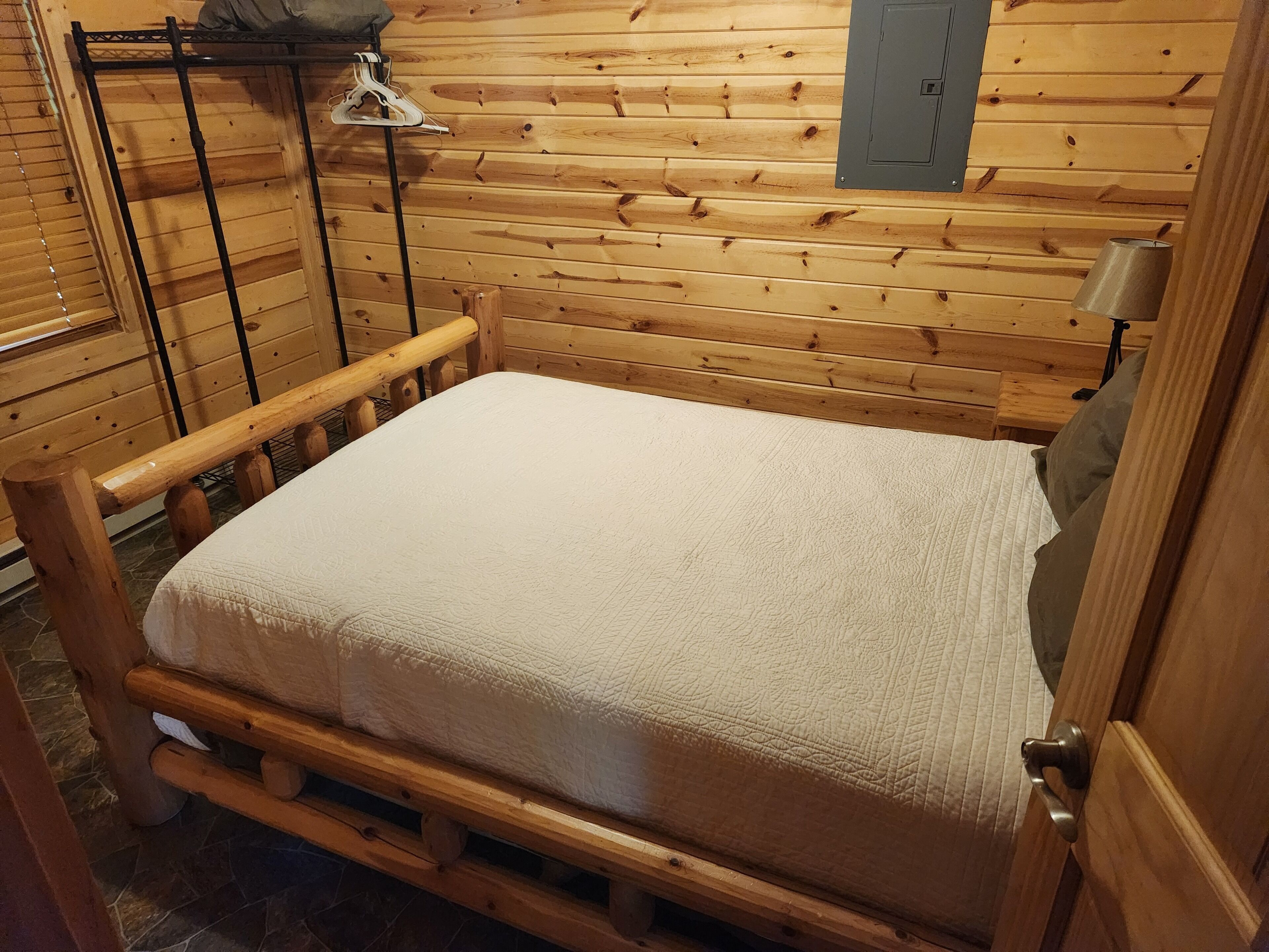 Un lit en bois avec un matelas matelassé, dans une pièce aux murs en bois et à la porte en métal.