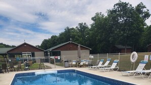 Une piscine rectangulaire dont le bord est recouvert de carreaux, entourée de chaises longues et d’une clôture.