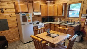 Een houten keukentje met een stenen vloertegel, houten kastjes, een koelkast, fornuis en een eettafel met stoelen.
