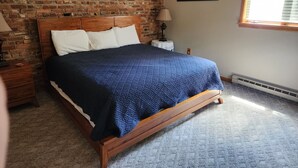 Ein Schlafzimmer mit Ziegelwand, Holzbettgestell, blauer Steudecke, einer weißen Lampe und einem Bild an der Wand.
