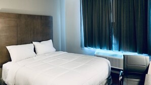 Une chambre d’hôtel avec un grand lit, une tête de lit, un bureau avec une chaise et une fenêtre avec des rideaux.