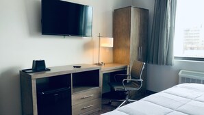 Une chambre d’hôtel comprenant un lit, un bureau avec une chaise, une télévision, une armoire et une fenêtre avec des rideaux.
