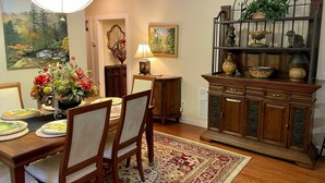 A dining area with a wooden table, chairs, a chandelier, a decorative cabinet, and a rug.