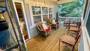 A covered porch with wooden flooring, wicker chairs with red cushions, and a chandelier.