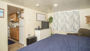 Ein Schlafzimmer mit Bett, Schminktisch, Fernseher und Fenster mit Baumdekor.