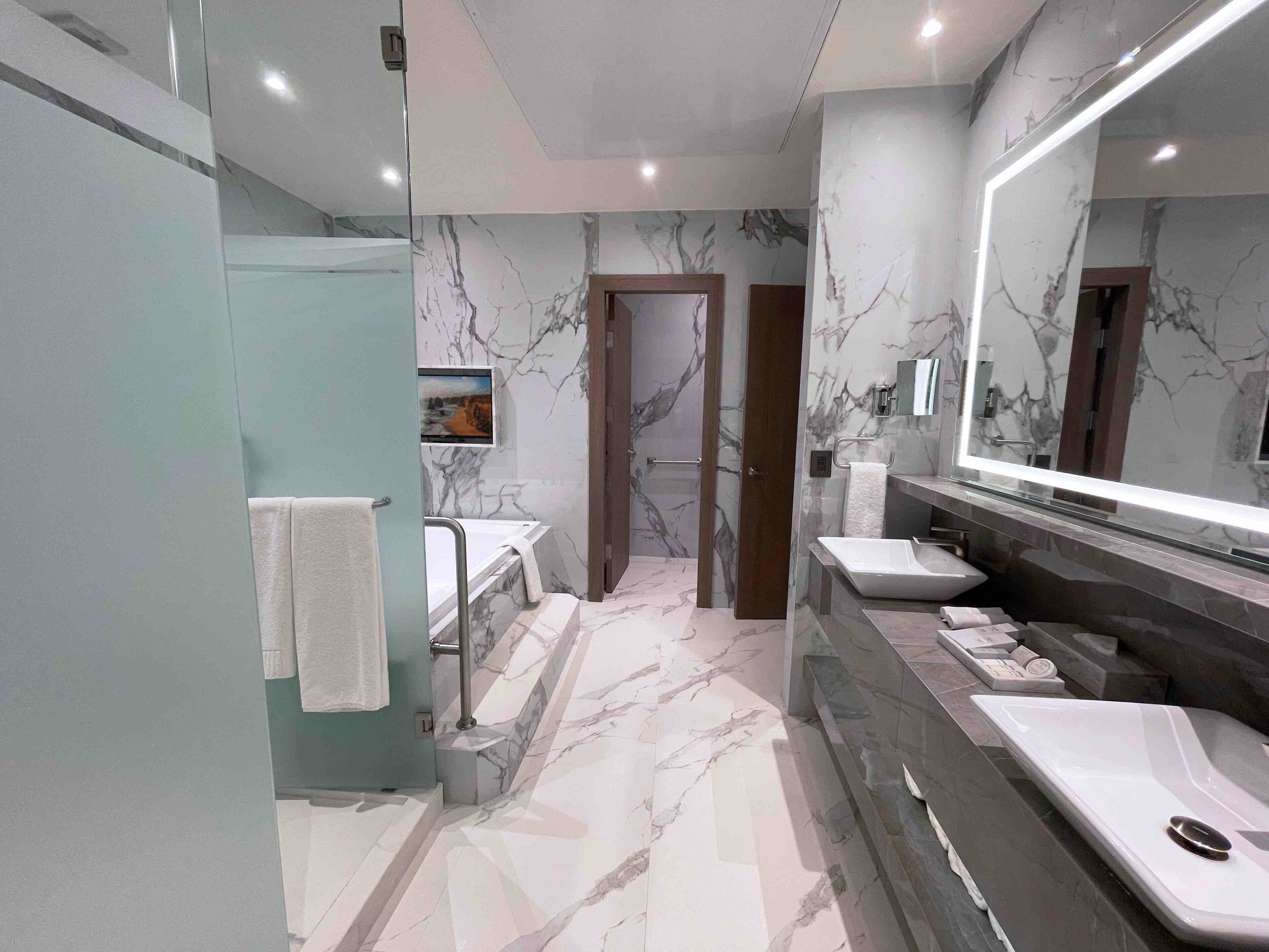 Un baño moderno con paredes de mármol, un espejo grande y una cabina de ducha de vidrio.