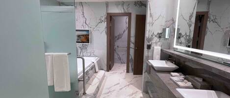 Un baño moderno con paredes de mármol, un espejo grande y una cabina de ducha de vidrio.