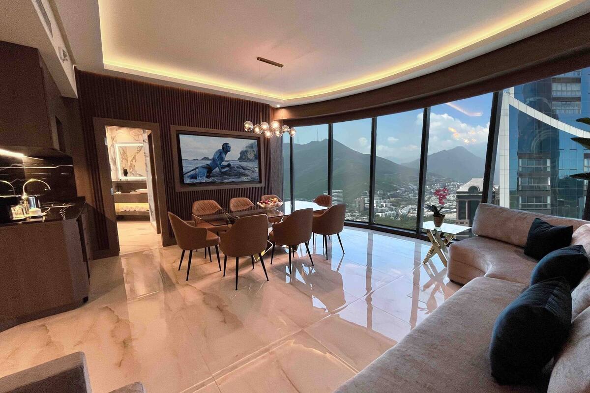 Een moderne woonkamer met een eethoek, een grote televisie en uitzicht op de stad.
