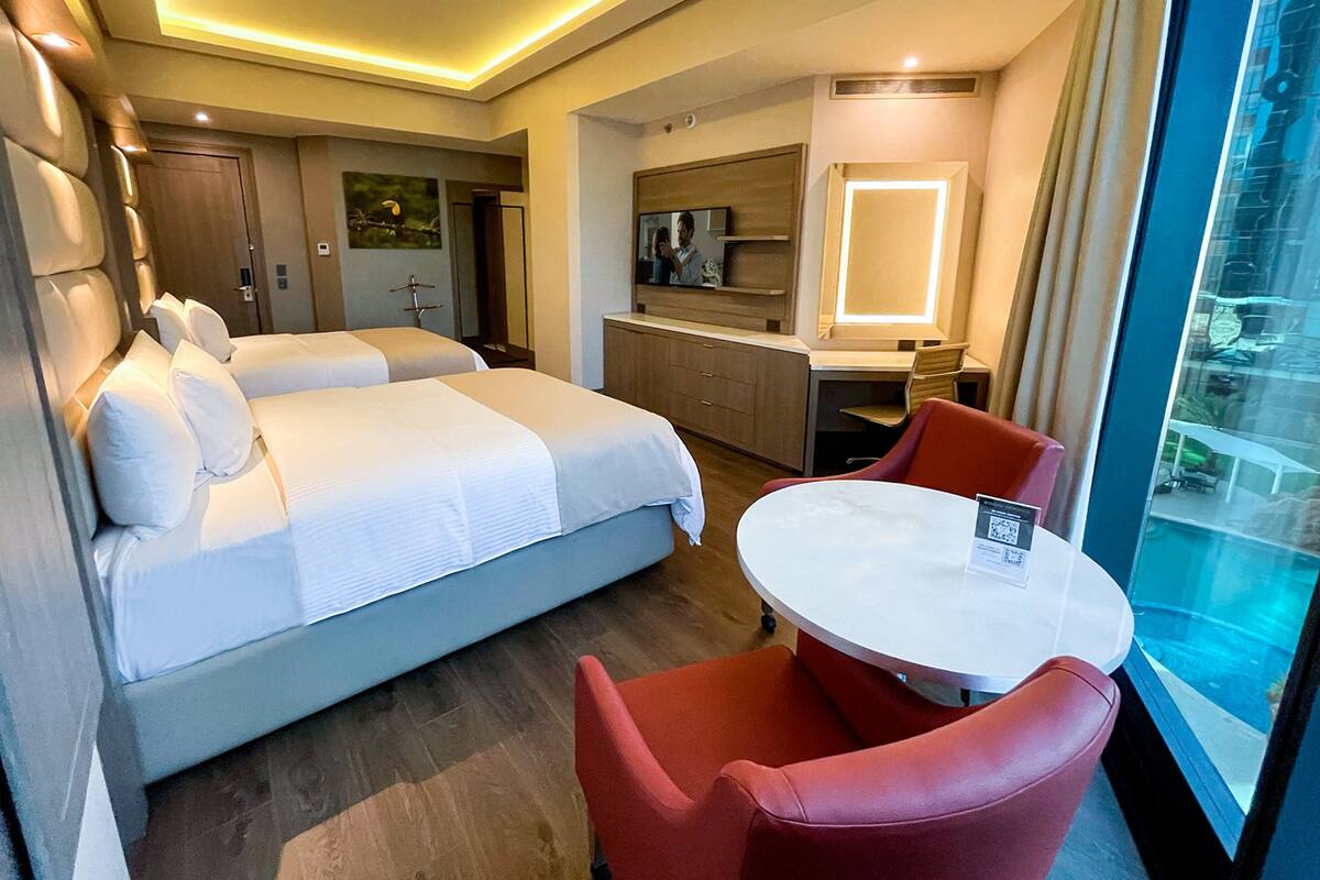 Een hotelkamer met twee bedden, een bureau, een stoel, een spiegel en een raam met uitzicht.