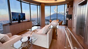 A modern living room with a large TV, comfortable seating, and a view of a cityscape and mountains. - Safi Royal Luxury Metropolitan (San Pedro Garza García)