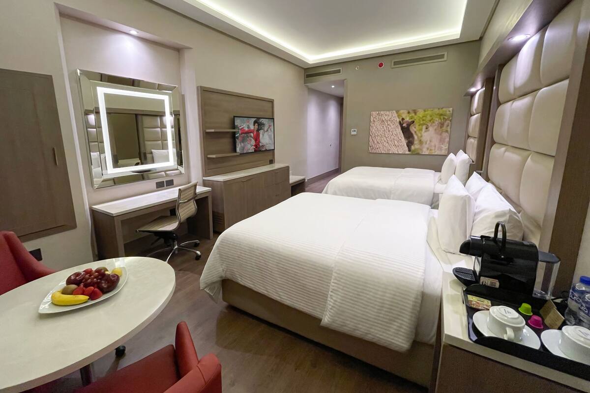Hotelkamer met een bed, een bureau, een stoel, een ronde tafel met fruit en een minibars kastje.