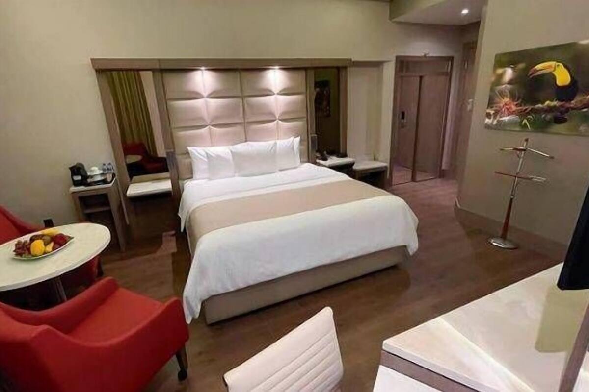 Een hotelkamer met een groot bed, een klein bureau met stoel, een eettafel met stoelen en een schilderij aan de muur.