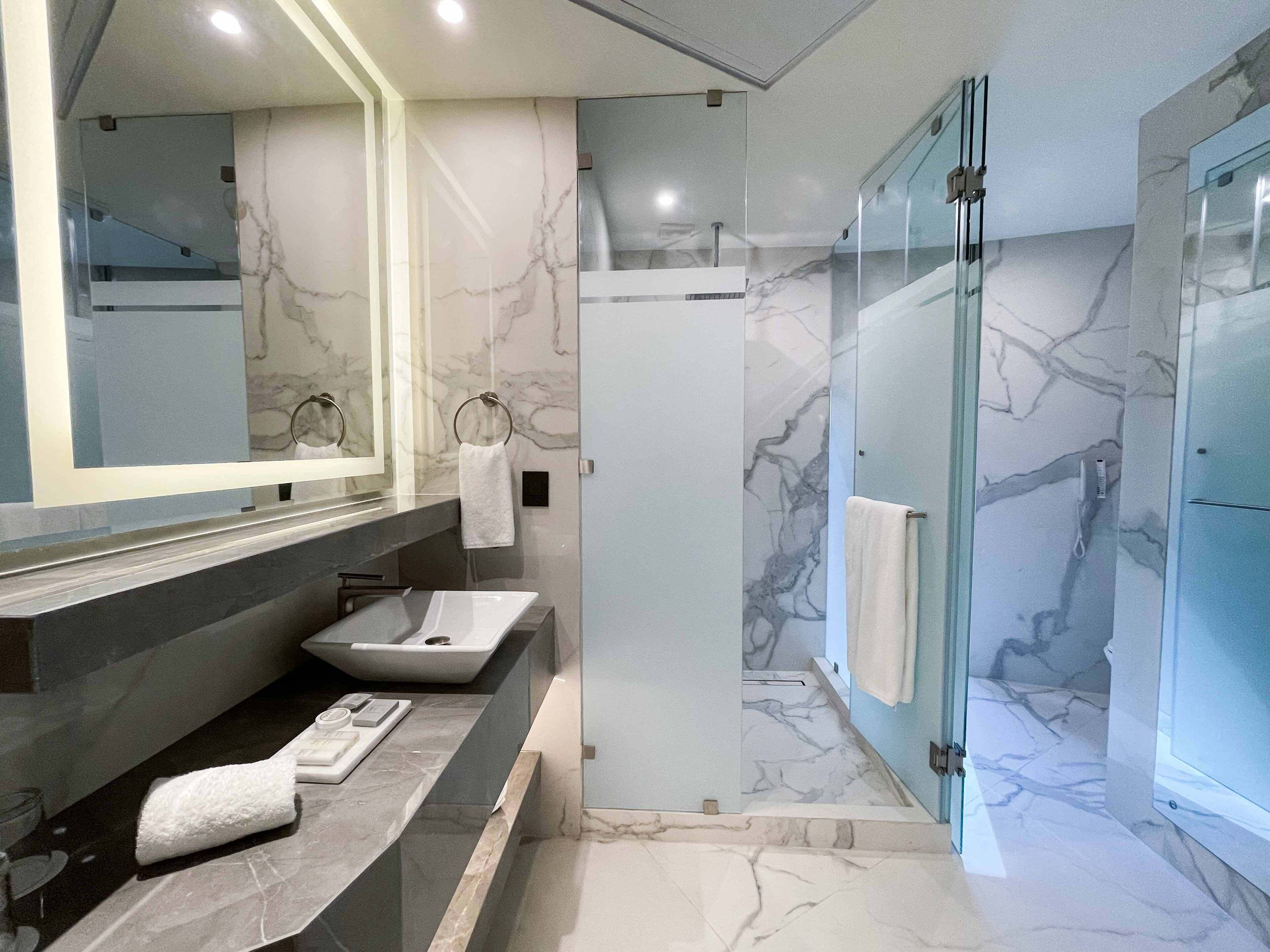 A modern bathroom with a marble vanity, a glass-enclosed shower, and a large mirror.