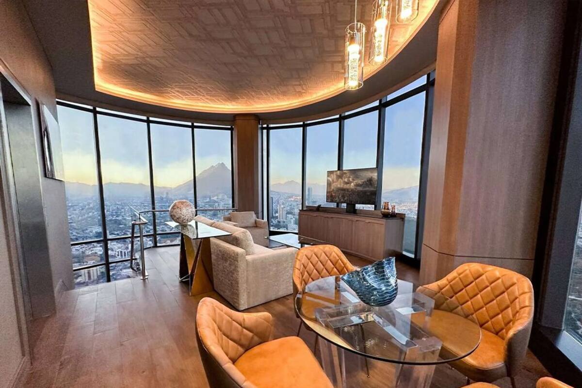 Een moderne woonkamer met een glazen tafel, leren fauteuils, een bank en een televisie.