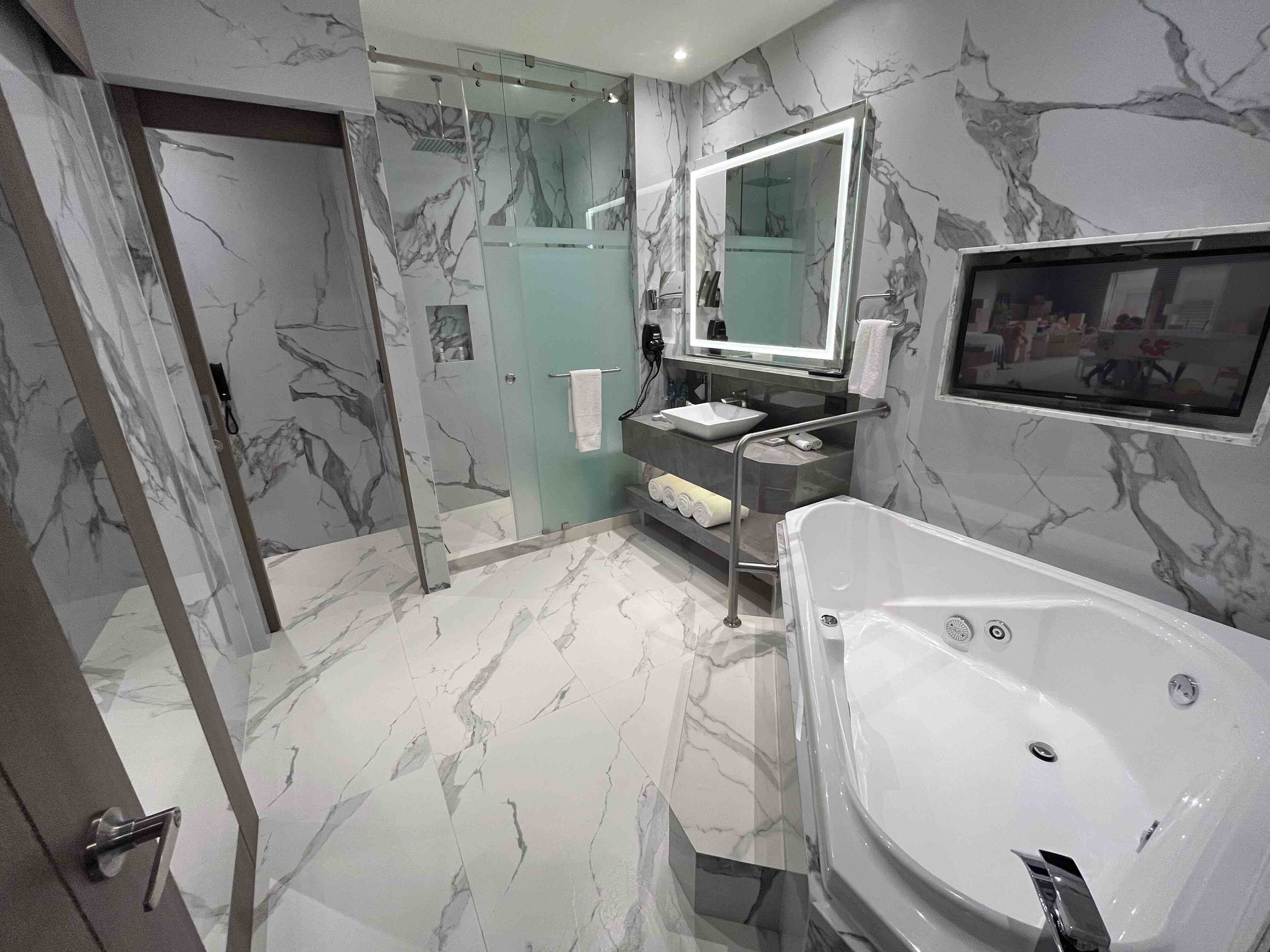 Un bagno moderno con una vasca da bagno ampia, una cabina doccia in vetro e un rivestimento murale effetto marmo.