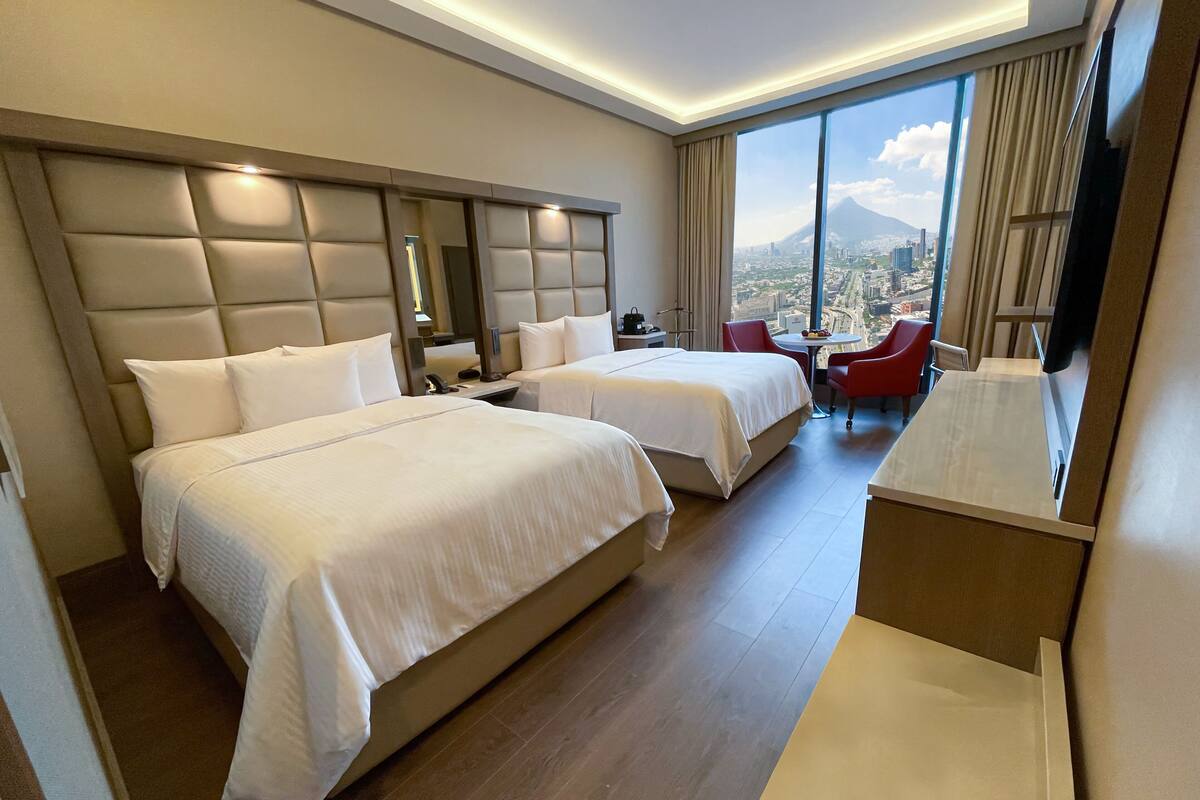 Een hotelkamer met twee bedden, een televisie, een bureau en uitzicht op een stadsgezicht.