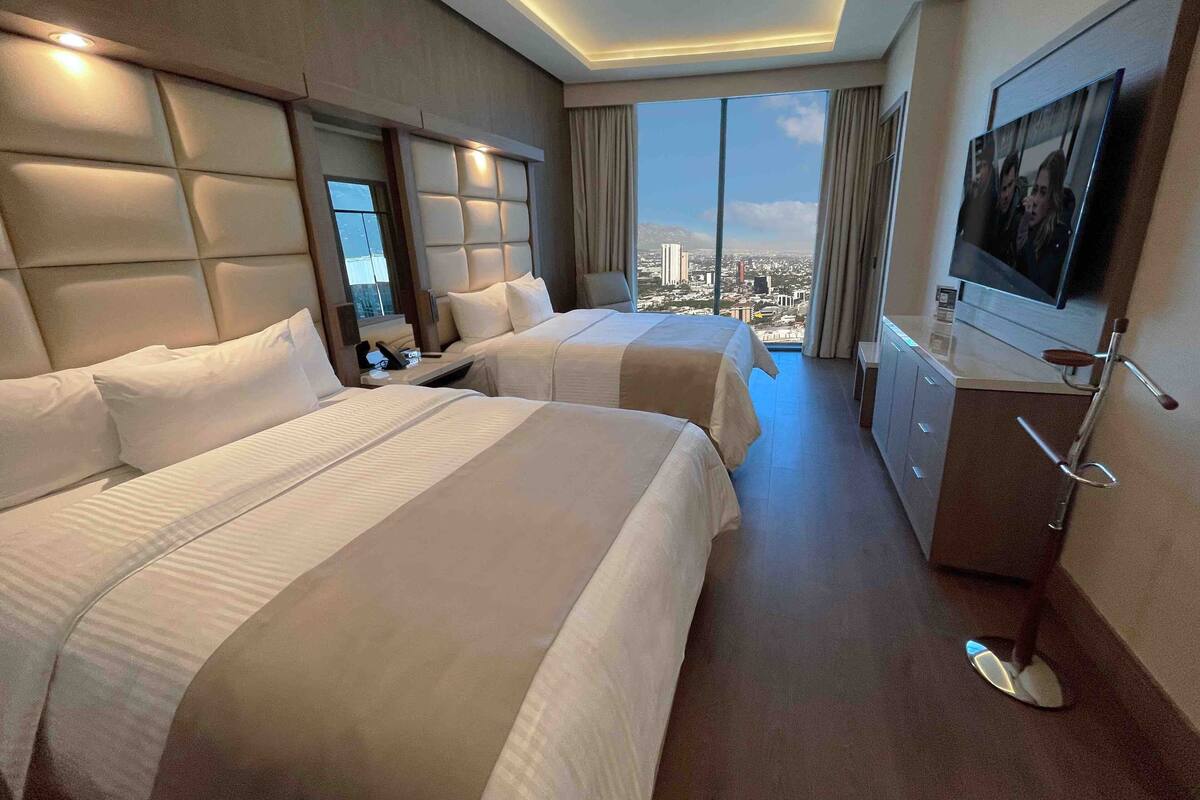 Een hotelkamer met twee bedden, een televisie en uitzicht over de stad.