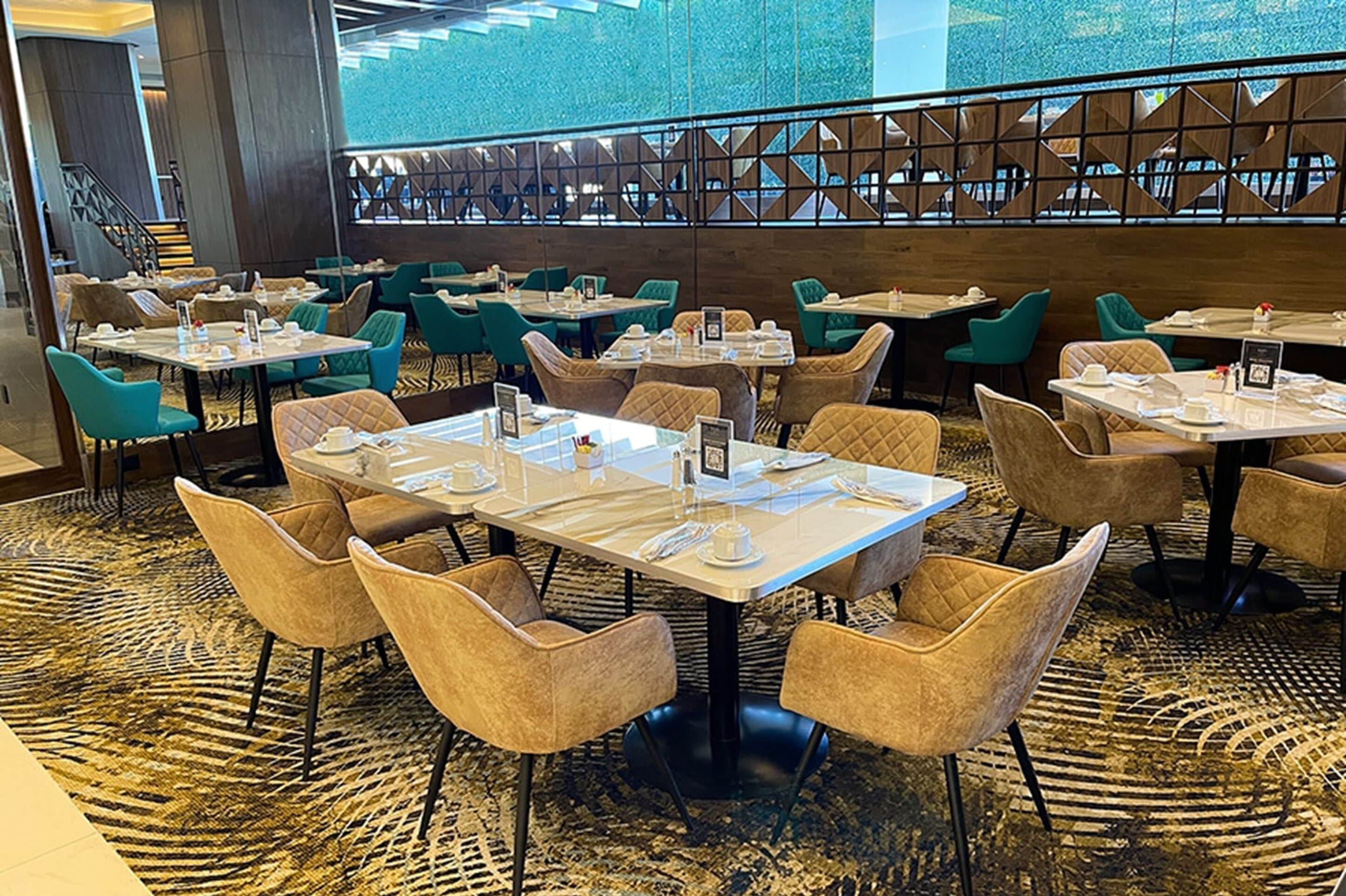Un comedor amplio con varias mesas y sillas, una alfombra estampada y una pared decorativa con motivos geométricos.