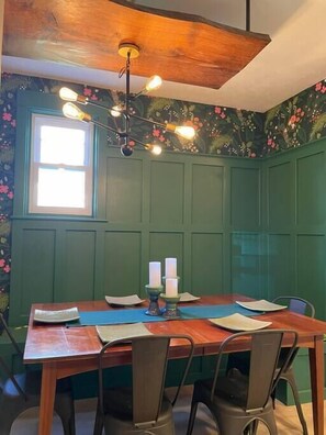 Ein Essbereich mit Holztisch, vier Stühlen, einer Kandelaberleuchte und grünen Wänden mit floralem Wandpapier.