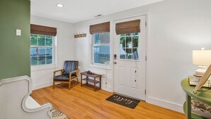 A room with a wooden floor, a green accent wall, a white door, and a window with a view of trees.