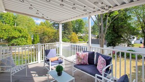 A covered outdoor seating area with white railings, a bench, and a table with a small plant.