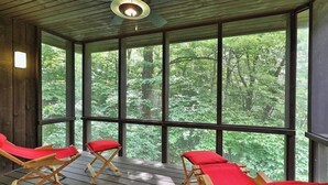 A wooden deck with four red lounge chairs facing a large window overlooking a forest.
