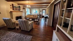 A spacious living room with a fireplace, a sofa set, and a dining area. - Twin River Stone Cottage - 7 BR/Sleeps 20 (Norfork)