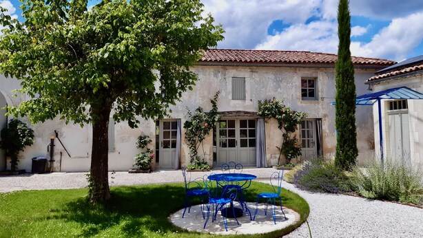 A rustic house with a garden, a patio with blue metal chairs, and a tall tree. - Between Landes and Sauternes, a cosy gîte! (Préchac)