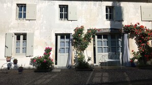 A two-story building with a white facade, multiple windows with shutters, and a tiled roof. There are potted plants and a bicycle parked in front. - Between Landes and Sauternes, a cosy gîte! (Préchac)
