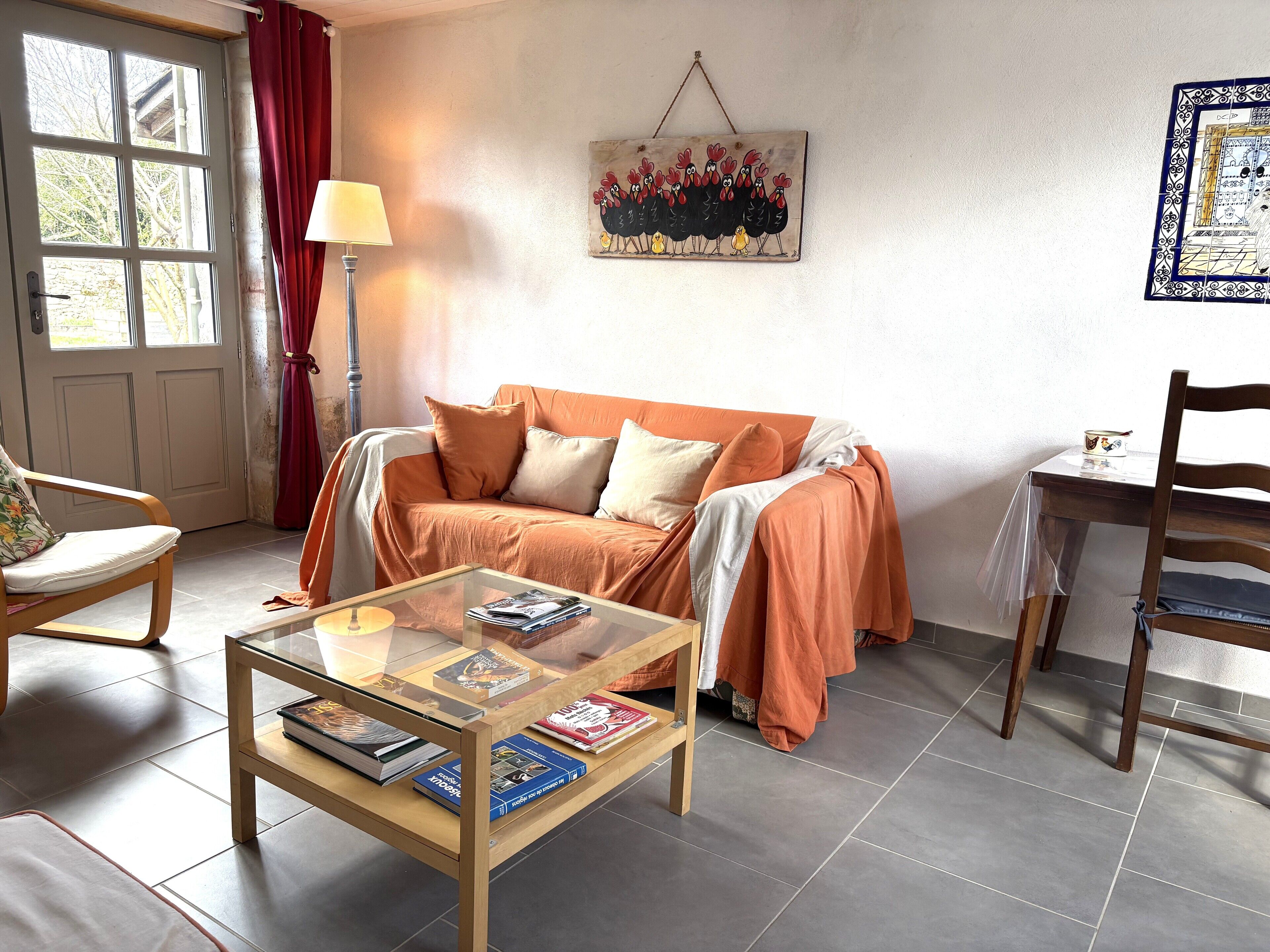 Una sala de estar con un sofá, una mesa de centro de vidrio con libros, una lámpara y un cuadro en la pared.