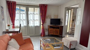 A living room with a sofa, a coffee table with books, a TV on a wooden cabinet, and a door leading to another room. - Between Landes and Sauternes, a cosy gîte! (Préchac)